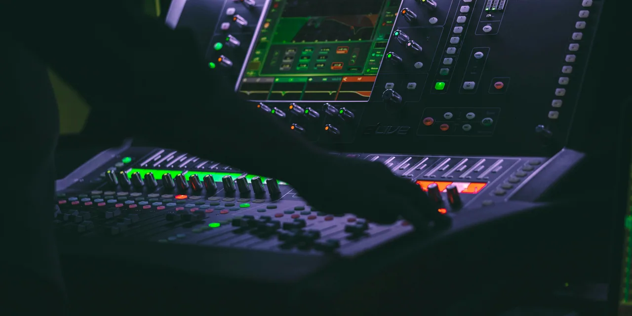 Engineer's hands working faders and knobs on an illuminated digital mixing console.