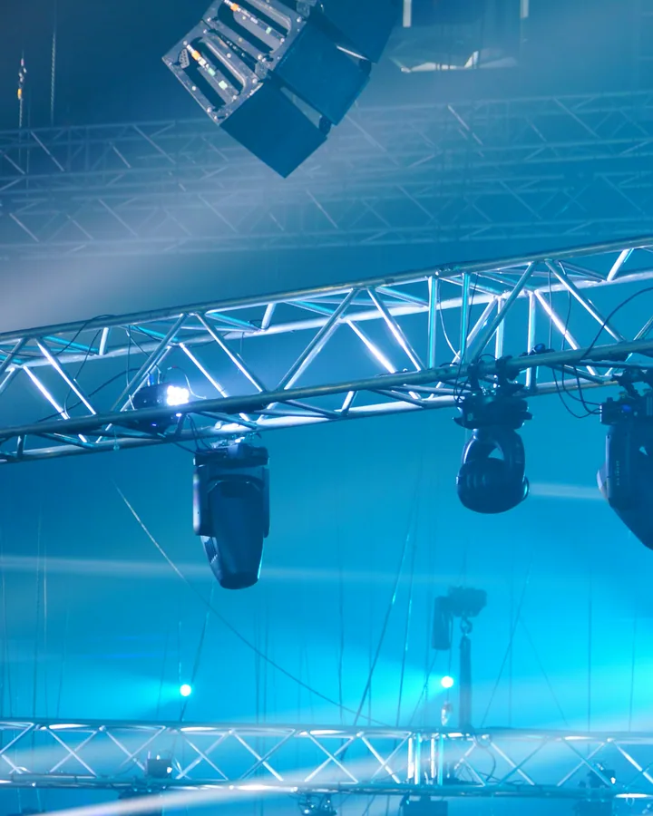 Lighting truss with moving fixtures cutting blue beams through theatrical haze.
