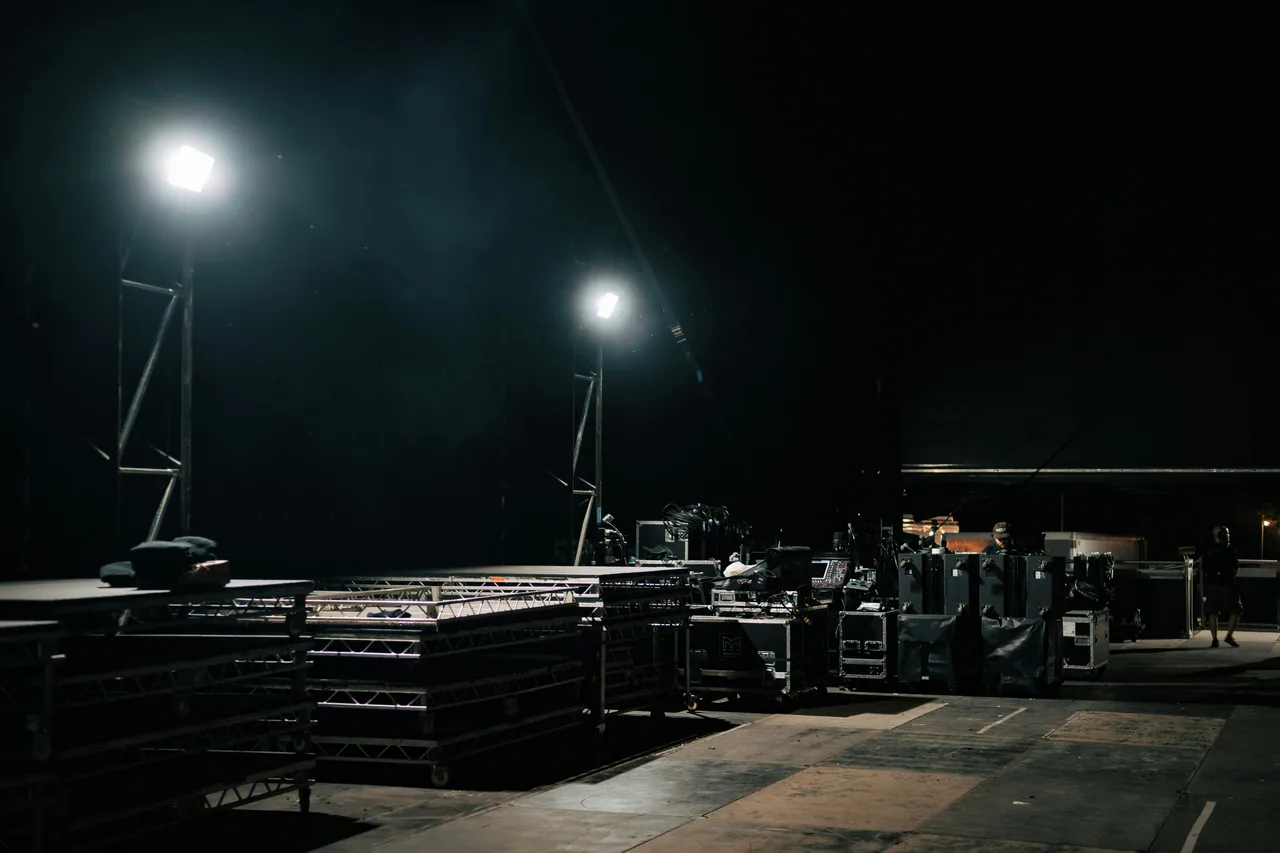 Backstage staging area at night — flightcases, truss, work lights, ready for load-in.